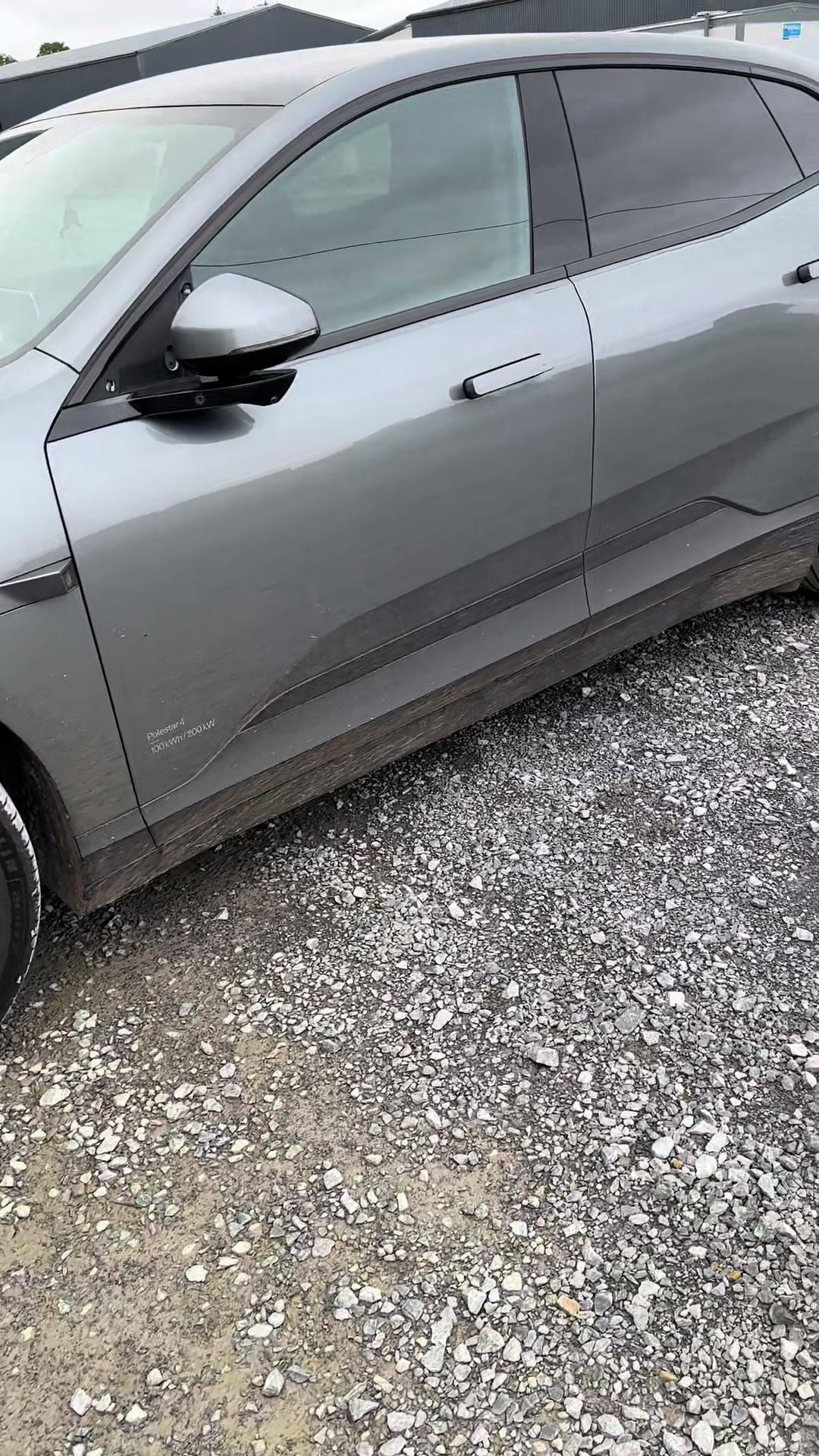Side profile of a clean grey car parked on a gravel lot.
