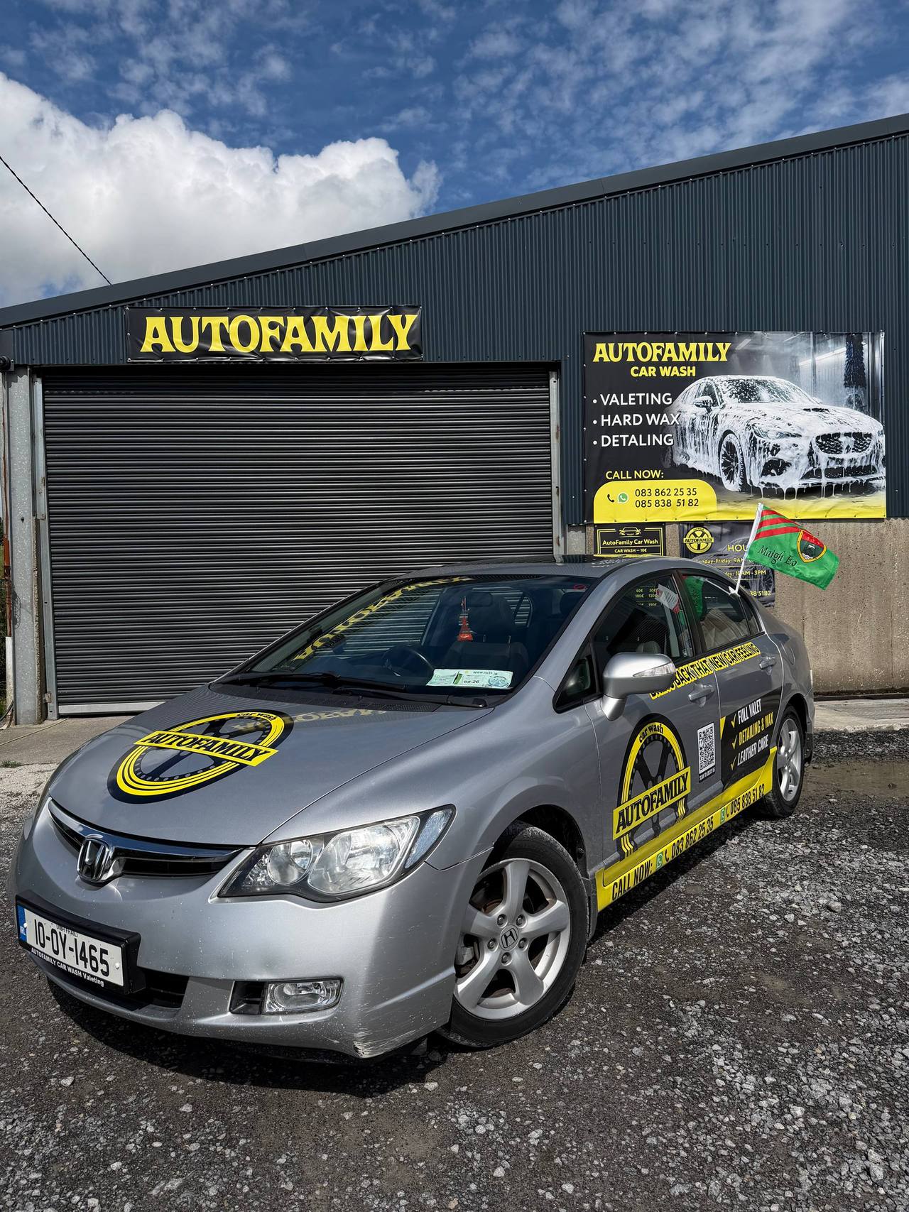 Silver Honda car with yellow branding parked outside AutoFamily car wash facility