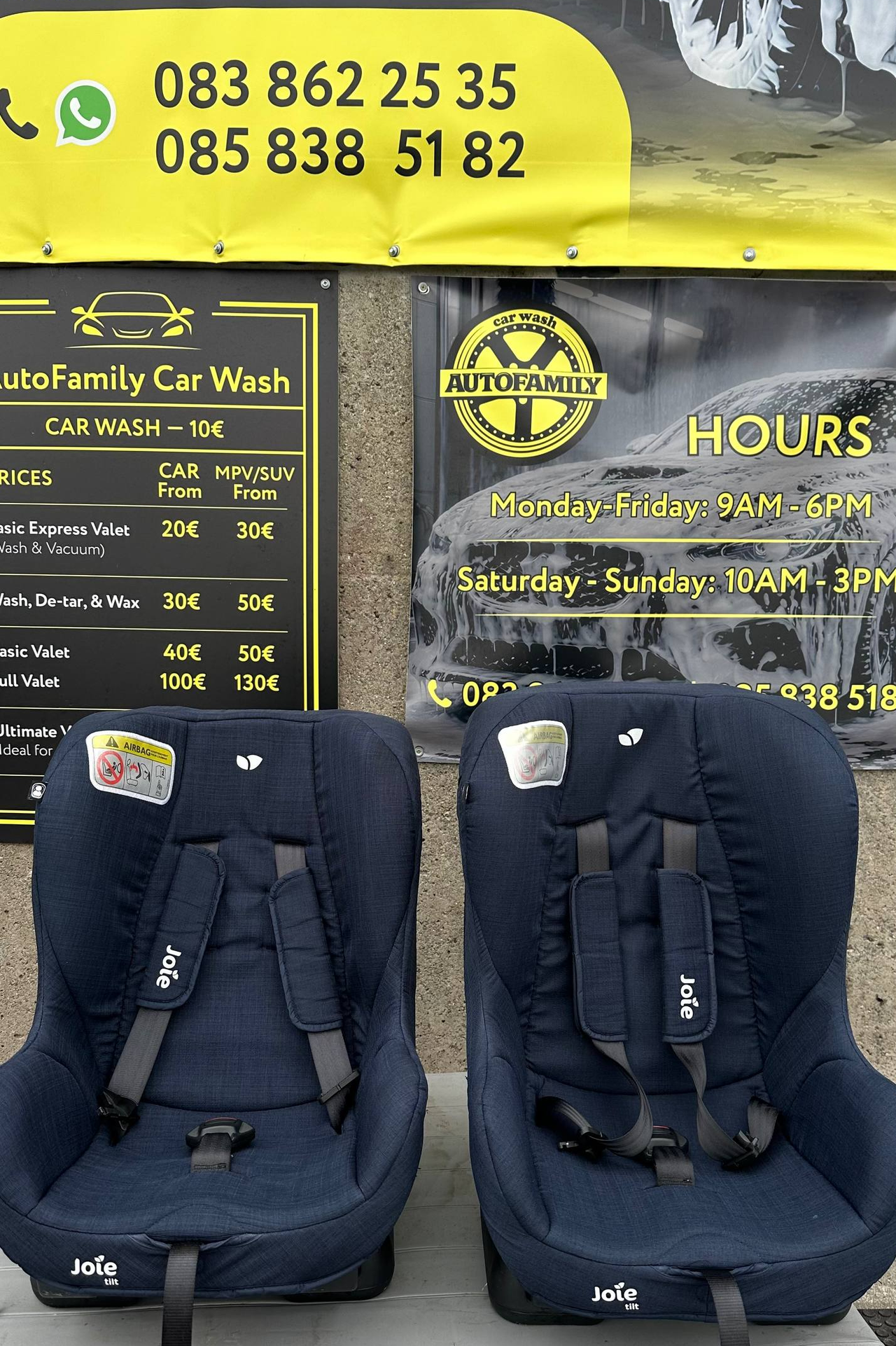 Two dark blue child car seats displayed in front of a car wash storefront