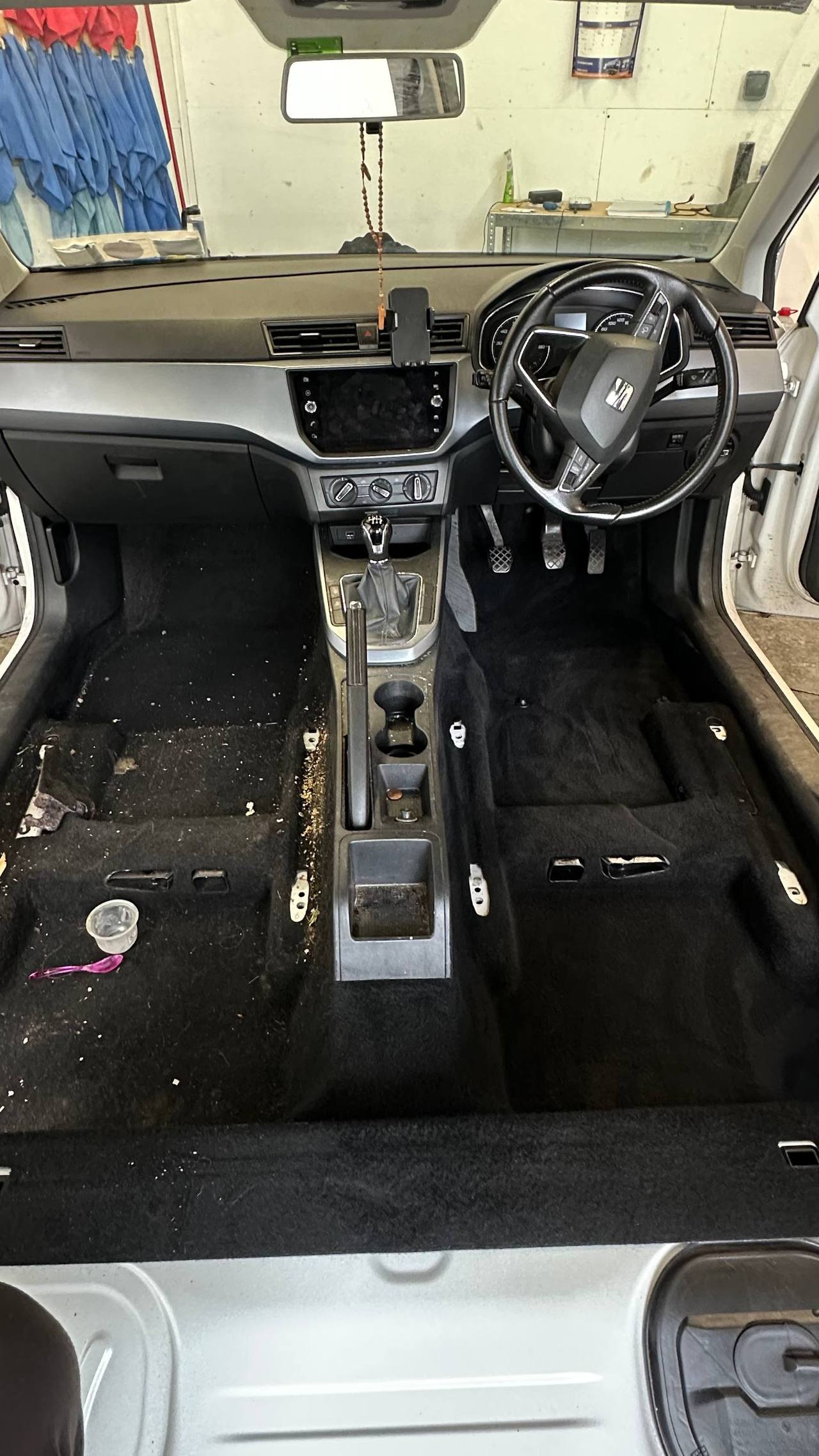Car interior with steering wheel, dashboard, and black floor mats in a garage setting